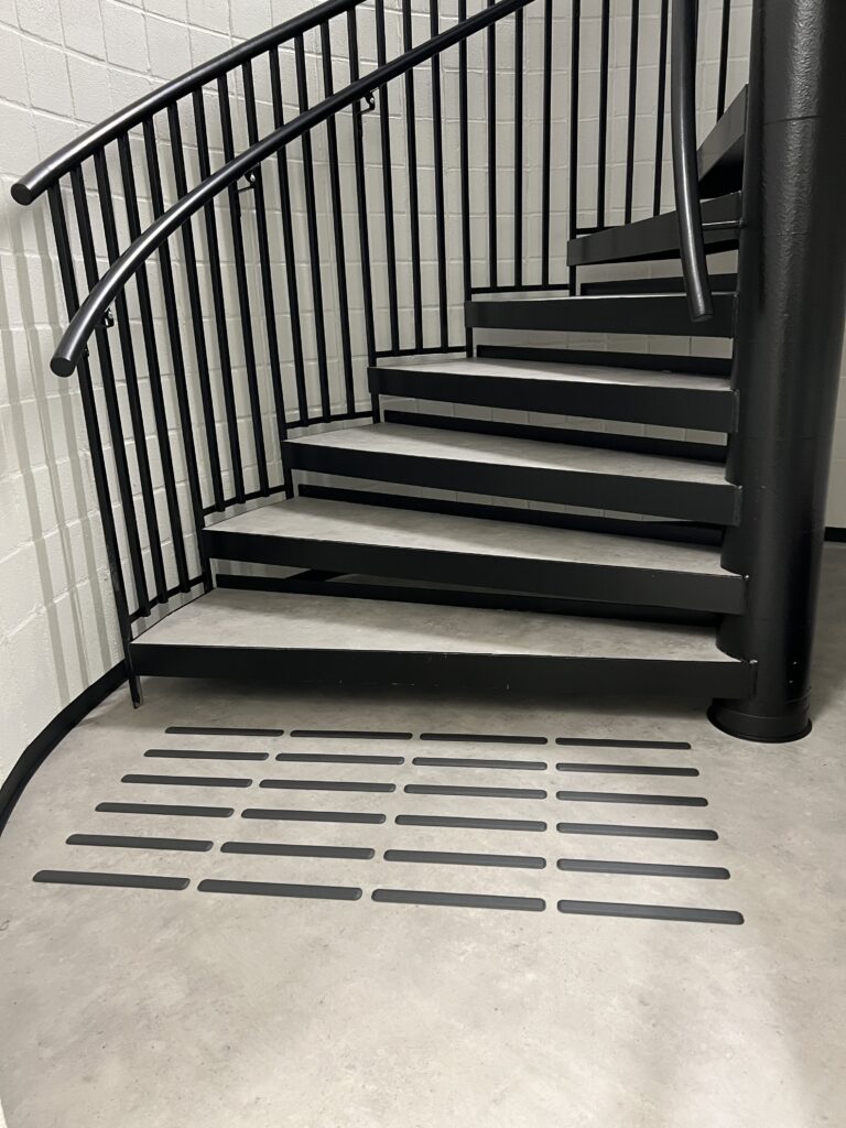 Et oppmerksomhetsfelt ved en inngang, laget med taktile linjer i kontrastfarge. Dette feltet hjelper personer med synsnedsettelser å identifisere viktige punkter i bygningen, som innganger eller høydeforskjeller.